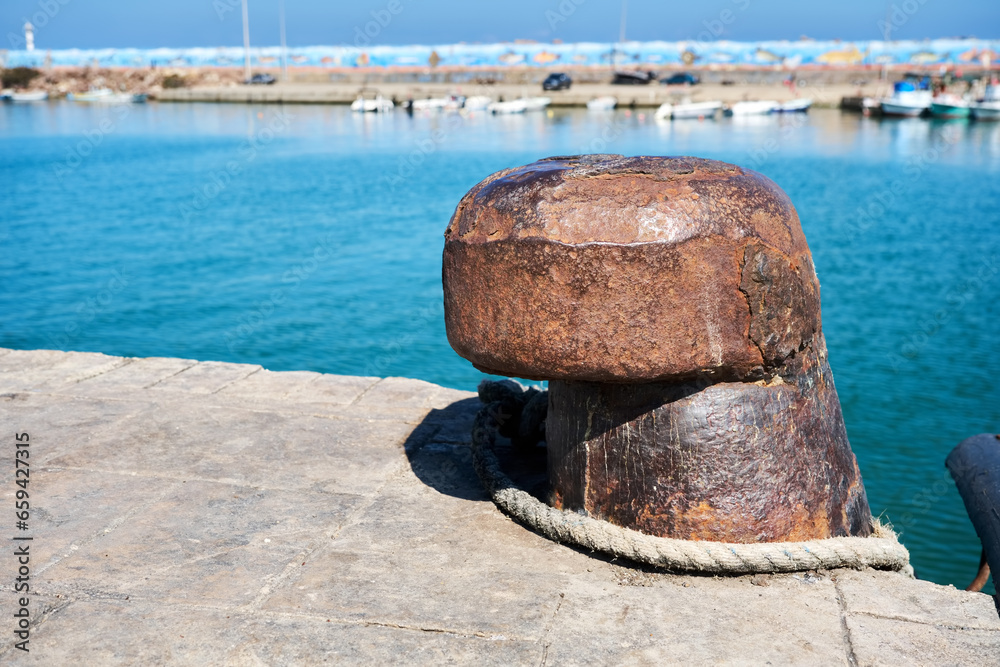 Rusty old steel mooring bollard with sea and fishing boats background. Rusty old steel mooring bollard with sea and fishing boats background.