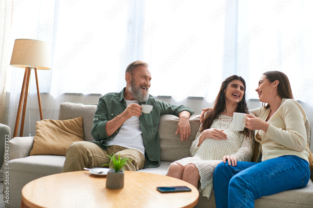 lgbt family and father sitting on sofa laughing and drinking tea, in vitro fertilization concept lgbt family and father sitting on sofa laughing and drinking tea, in vitro fertilization concept