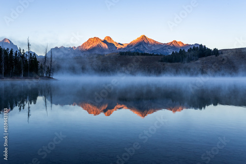 Redfish lake in Idaho in dawn. Calm water covered by mist. Mountains range is reflecting in lake water