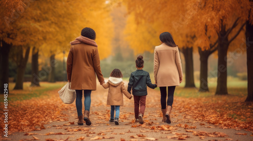 Two women with children walking in the park fall autumn yellow leaves and trees