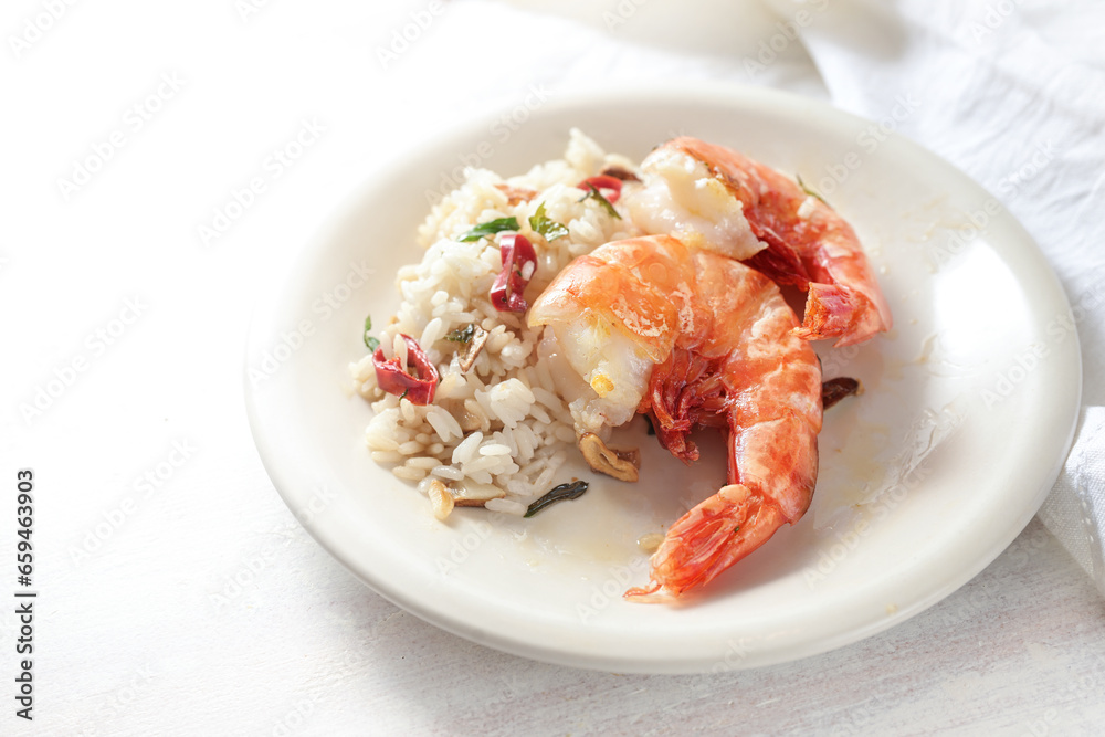 Fried tiger prawns or shrimps and rice spiced with garlic, red chili pepper and herbs on a white plate and a light background, homemade seafood meal, copy space, selected focus Fried tiger prawns or shrimps and rice spiced with garlic, red chili pepper and herbs on a white plate and a light background, homemade seafood meal, copy space, selected focus