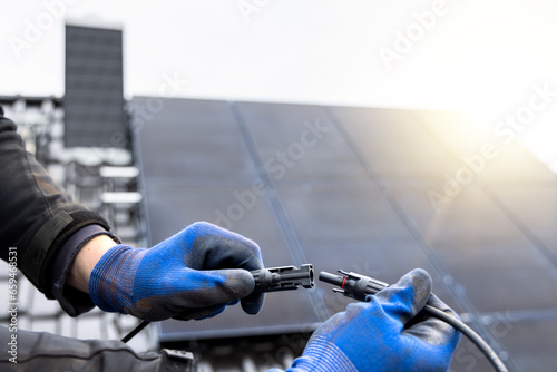 Hands holding solar panel connector cables on a roof of a house