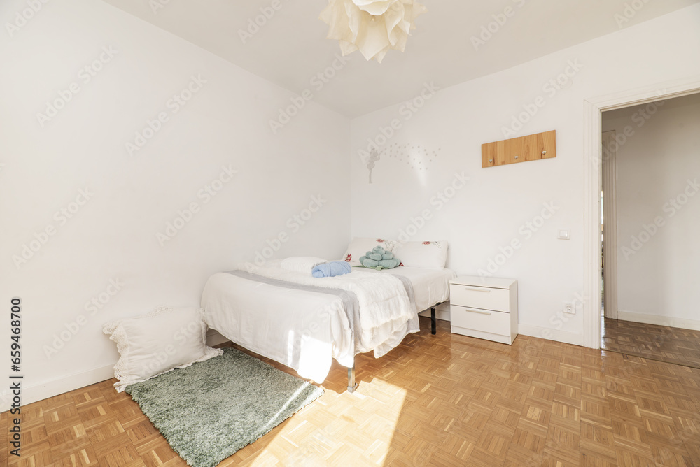 Bedroom with double bed with chess parquet floor, white bedside table with drawers, green long hair rug and towels on the bed Bedroom with double bed with chess parquet floor, white bedside table with drawers, green long hair rug and towels on the bed