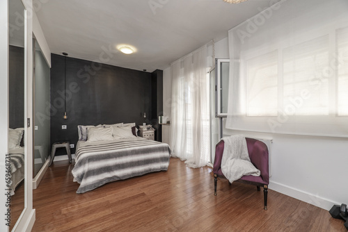 Double bedroom en suite, chest of drawers with white drawers, TV attached to the wall, balcony with aluminum and glass door, armchair upholstered in violet silk, wooden floors