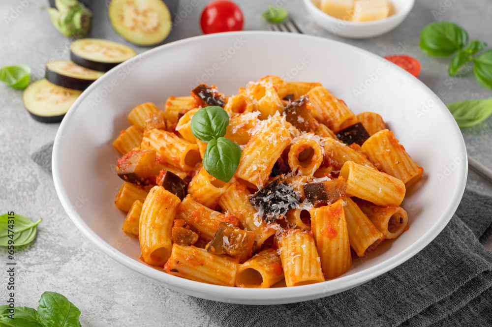 Pasta alla Norma. Italian pasta with eggplant, tomato sauce, cheese and basil in a gray concrete background. Comfort food.
