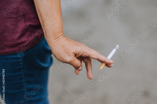 A cigarette with smoke in the hands of an elderly woman, a pensioner, a smoker. Photography, close-up portrait, smoking concept. © shchus