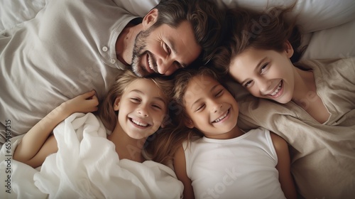 Family and love: top view, happy family teasing each other in bed, parents and children, warm white bedroom, hugs