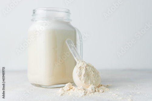 Glass jar of protein milkshake drink or smoothie and whey protein powder in measuring spoon on a white background. sport nutrition, bodybuilding food supplements photo