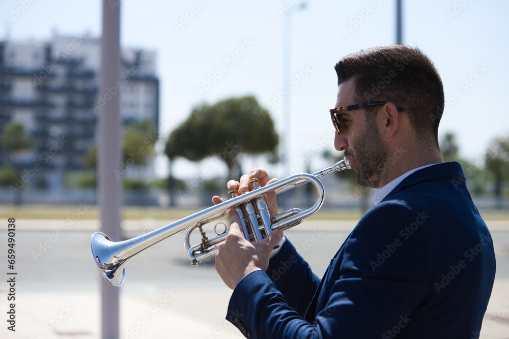 Obraz premium Handsome young businessman with a beard and a blue suit playing the trumpet. The man is a musician in his spare time and music is one of his great passions.