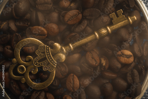 Golden vintage key on a background of hot coffee beans. An antique key against a background of coffee beans with smoke.