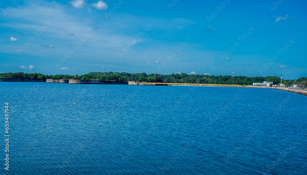 Blue sea with forest on the coast. Blue sky with white clouds.