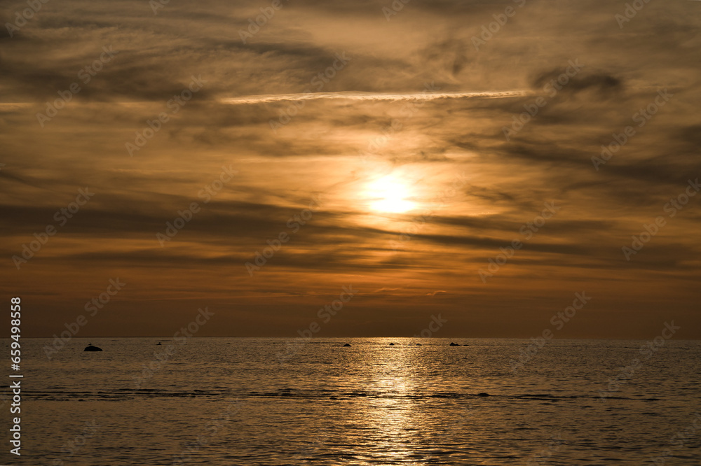 Sunset, illuminated sea. Sandy beach in the foreground. Light waves. Baltic Sea.