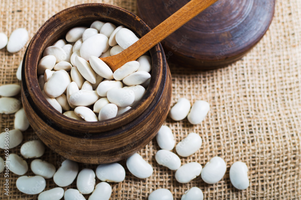 Mound of raw, white organic beans in wooden bowl, healthy and nourishing legume cuisine Mound of raw, white organic beans in wooden bowl, healthy and nourishing legume cuisine
