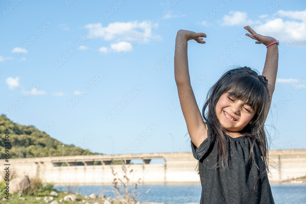 Hispanic girl on vacation at beautiful lake. Raising her arms very happily.
