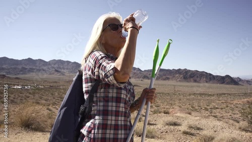 Woman is hiking hot are at deserts and she was tired and decide get drink water. Senior drinking water at rock place.
