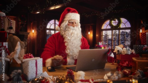 Arc Shot of Father Christmas Sitting and Using a Modern Laptop Computer. Santa is Browsing Online, Communicating with Clients, Managing a Successful Online Shopping Business with Gifts for Children photo