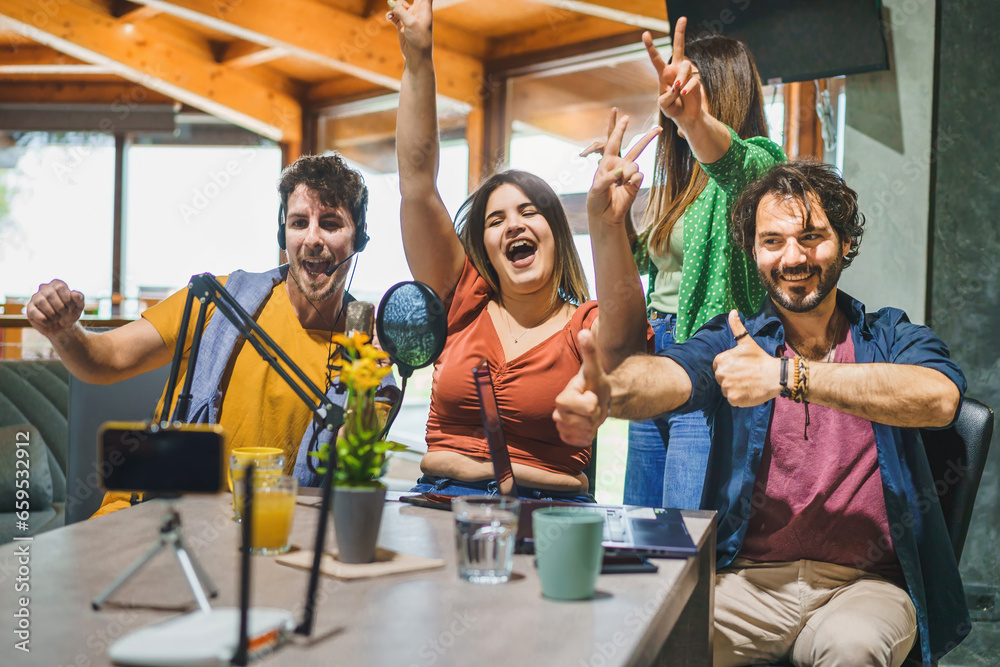 Four Friends Celebrate Victory During a Live Stream - Enthusiastic content creators cheer and gesture, engaging with their audience while recording a video blog using a smartphone and microphone. Four Friends Celebrate Victory During a Live Stream - Enthusiastic content creators cheer and gesture, engaging with their audience while recording a video blog using a smartphone and microphone.