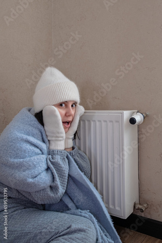 a warmly dressed woman sits near a radiator and is shocked by the lack of heating © phpetrunina14