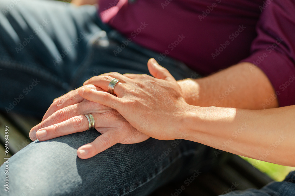Homosexual couple sitting on bench holding hands, selective focus on rings, closeup