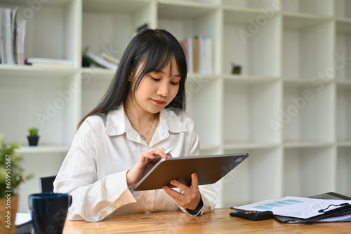 Pretty asian female office worker using digital tablet at her workplace