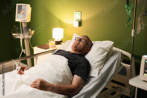 Portrait of a senior man peacefully asleep with an oxygen tube and glasses in hospital ward recovering