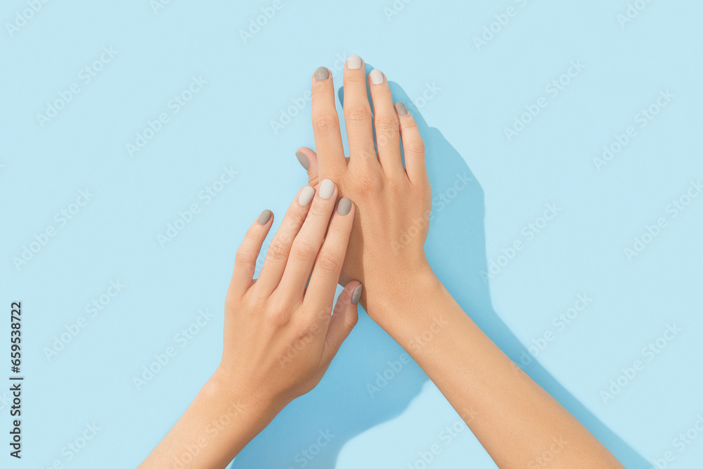 Womans hands with gray nail design on blue background