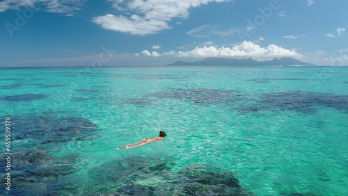 Woman snorkeling crystal clear turquoise water coral barrier reef, sunny day. Slim girl in bikini enjoy outdoor lifestyle travel summer holiday vacation. Tahiti, Polynesia. Aerial top view, drone shot