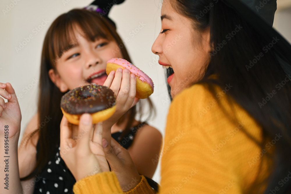 Happy family, cute little girl eating sweet donut with mother in kitchen. Halloween celebration and activity relationship in house Happy family, cute little girl eating sweet donut with mother in kitchen. Halloween celebration and activity relationship in house