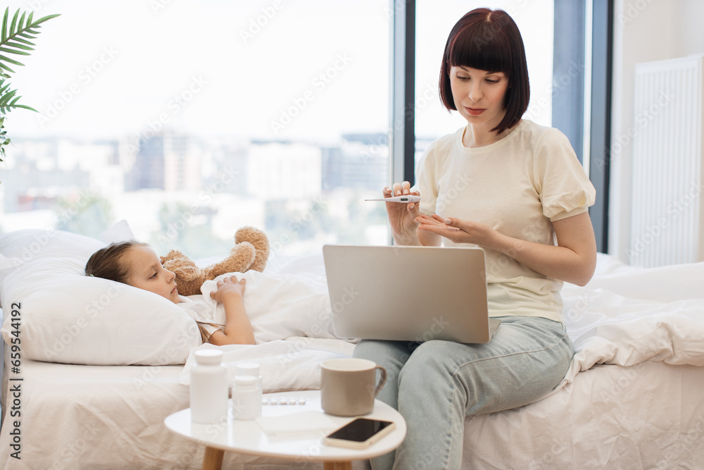 Caucasian mother sitting on bed with modern laptop and showing digital ...