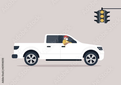 A senior driver in a pickup truck, casually steering with one arm hanging out of the window while they wait at the yellow traffic light