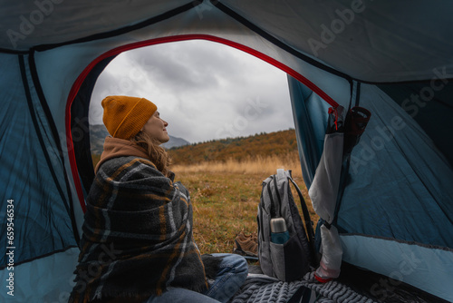 Young cheerful woman sitting in a tent while travelling. Hiking travel and trekking concept