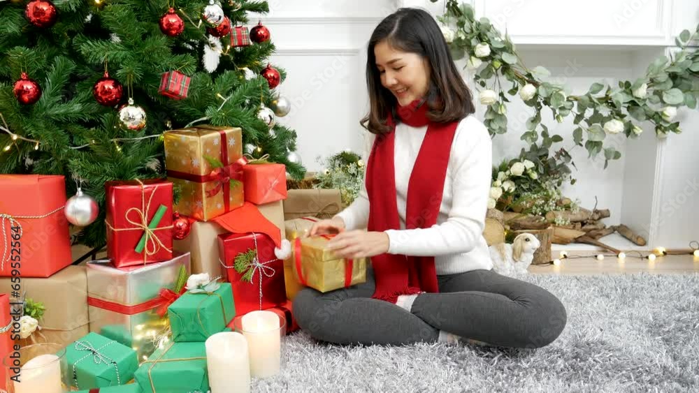 Close up woman hands wrap present gift in cozy living room. Woman wrapping christmas gift box under xmas tree. Asian woman decor bauble ball christmas tree in xmas holiday winter seasonal celebration Close up woman hands wrap present gift in cozy living room. Woman wrapping christmas gift box under xmas tree. Asian woman decor bauble ball christmas tree in xmas holiday winter seasonal celebration