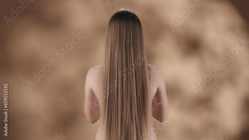 Framed against a blotchy background is a young woman with long and smooth white, russet hair. She is standing back with no outer clothing. Tossing her hair while the wind blows it around her