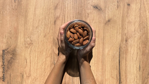 Child holding almond nuts on wooden background, top view. Place for text