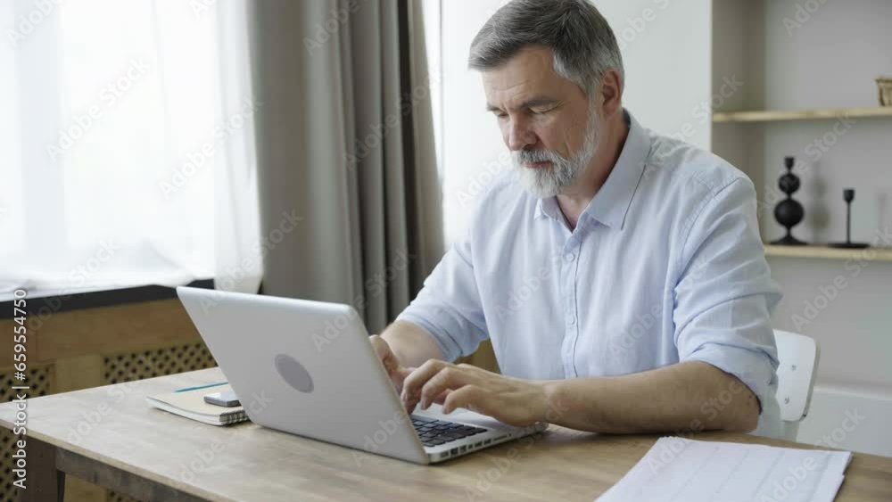 Older man working online with laptop computer at home sitting at desk. Home office, surfing internet Older man working online with laptop computer at home sitting at desk. Home office, surfing internet