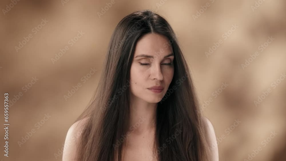 In the shot against a blotchy background is a middle-aged woman with long and smooth dark, black hair. She stares intently into the camera, the wind developing her hair. She smiles In the shot against a blotchy background is a middle-aged woman with long and smooth dark, black hair. She stares intently into the camera, the wind developing her hair. She smiles