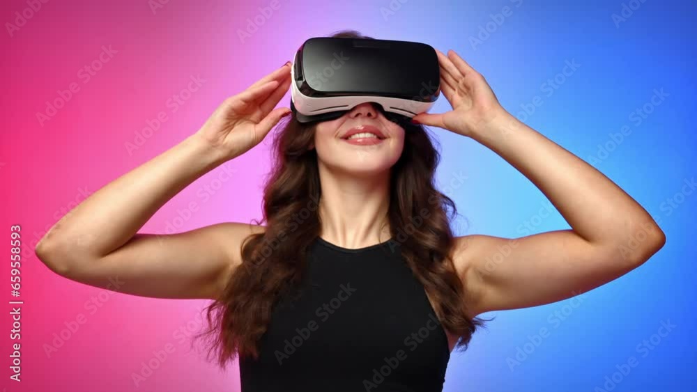 Young smiling woman in a tracksuit in virtual reality VR headset looking around in a studio with blue and red background Young smiling woman in a tracksuit in virtual reality VR headset looking around in a studio with blue and red background