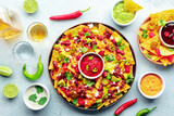 Loaded nachos. Mexican nacho chips with beef, overhead flat lay shot with guacamole sauce, cheese salsa, tequila drinks, limes, and chili peppers