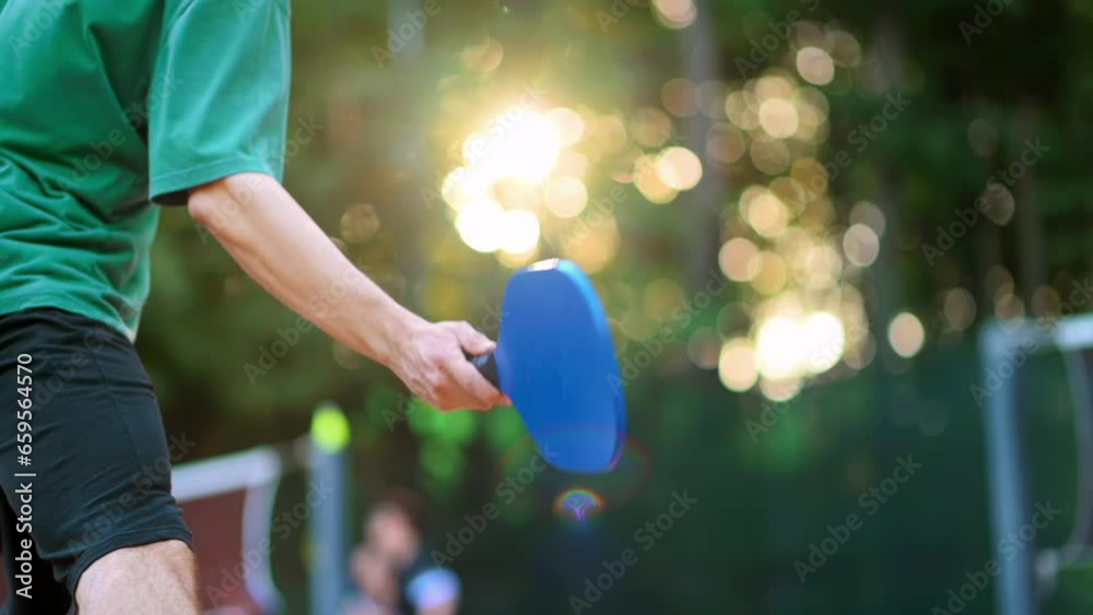 Man playing Pickleball, hitting the ball with a racket on an outdoor court. Slow motion
