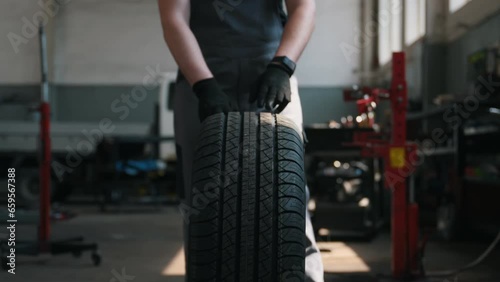 front view, the hands of a car mechanic rolling a wheel in the workshop