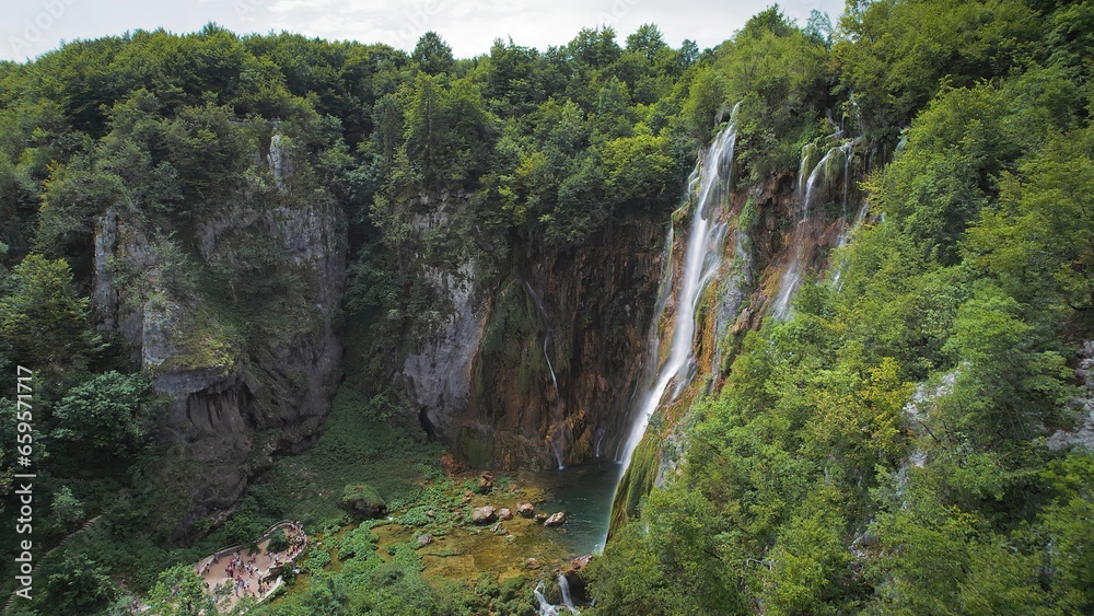 Amazing waterfall falling from a high cliff in lush green forest. Mountain cascade with clear water.