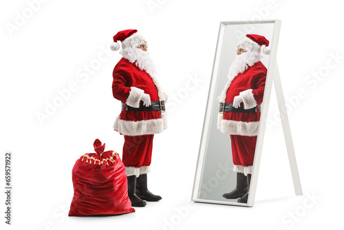 Full length profile shot of santa claus standing next to his sack and looking at a mirror