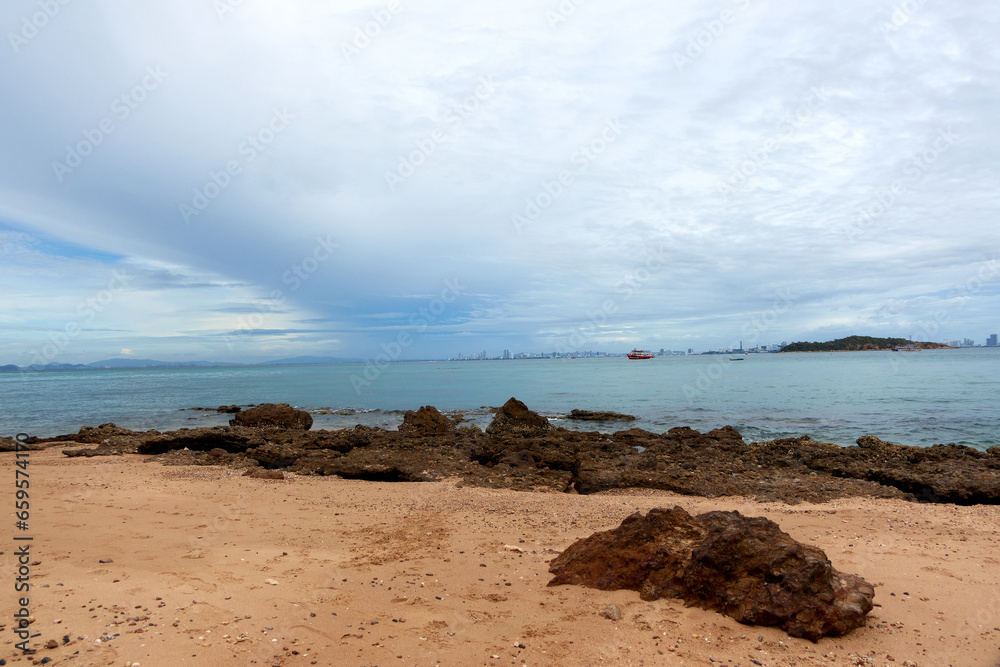 Landscape of rocky beach and sea with distant mountains and islands, blue sky.