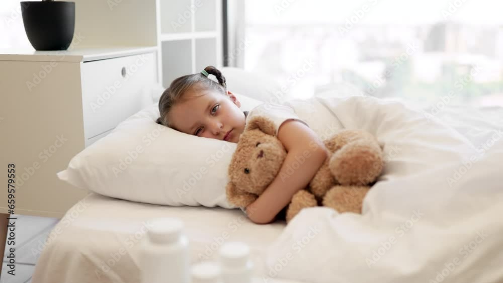 Tired caucasian little girl lying in soft bed with teddy bear in embrace and feeling sick. Coffee table with pills and thermometer standing near. Health care and disease concept. Tired caucasian little girl lying in soft bed with teddy bear in embrace and feeling sick. Coffee table with pills and thermometer standing near. Health care and disease concept.