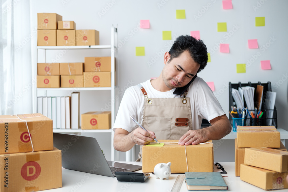 Asian man checking order and customer's details and addresses on laptop or box in order to prepare for shipping according to the information, Online shopping SME entrepreneur