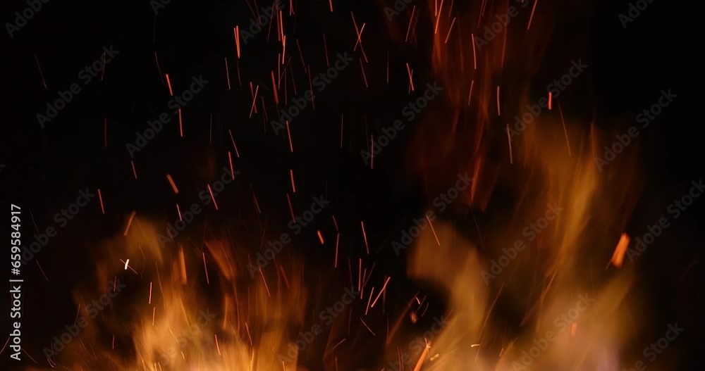 Fire and sparks at night close-up, slow motion. The flames of burning wood log fire on black background