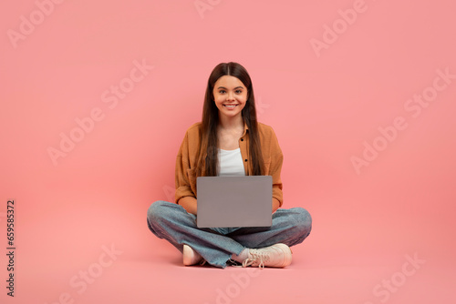 Smiling Teen Girl With Laptop Sitting On Floor Over Pink Background
