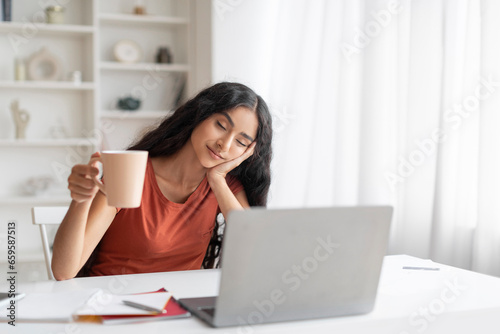 Sleepy millennial hindu businesswoman sitting at workplace with closed eyes