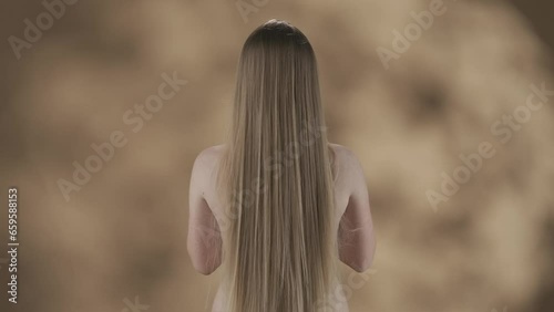 Framed against a blotchy background is a young woman with long and smooth white, russet hair. She is standing back with no outer clothing. Tossing her hair while the wind blows it around her HDR photo