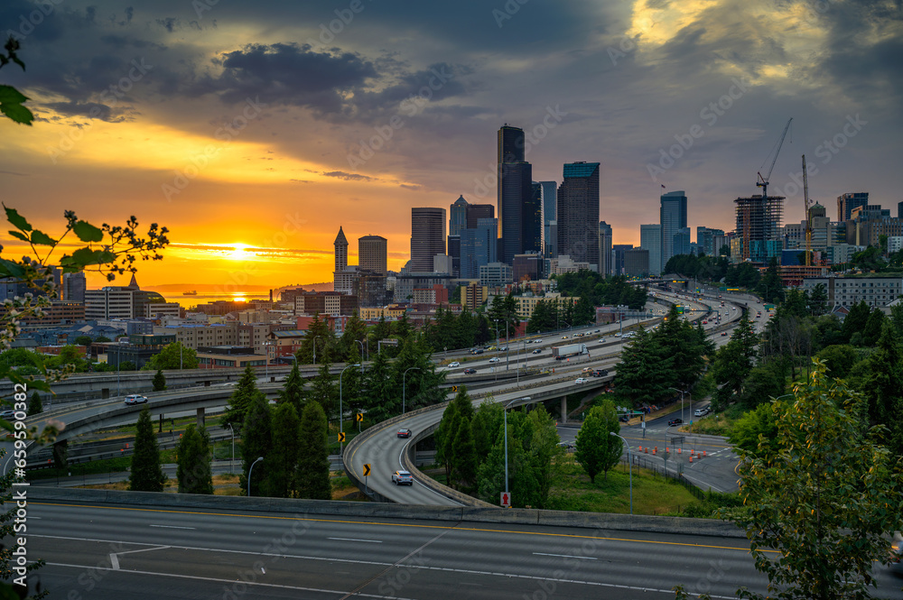 Fototapeta premium Dramatic sunset over the Seattle downtown skyline, with traffic on the I-5 and I-90 freeway interchange, viewed from Dr. Jose Rizal Bridge.